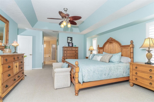 bedroom with light carpet, a tray ceiling, ceiling fan, and ensuite bathroom