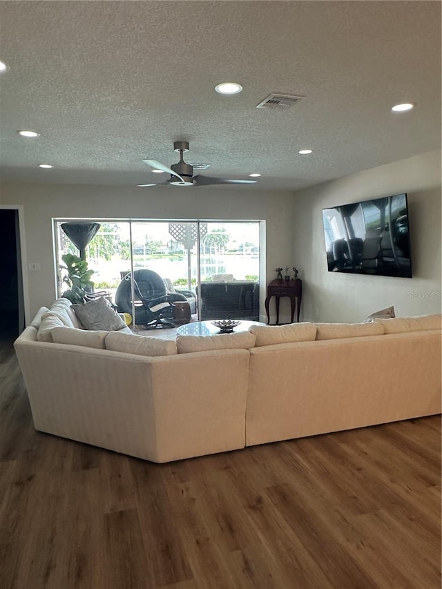 living room featuring dark hardwood / wood-style flooring, ceiling fan, and a textured ceiling