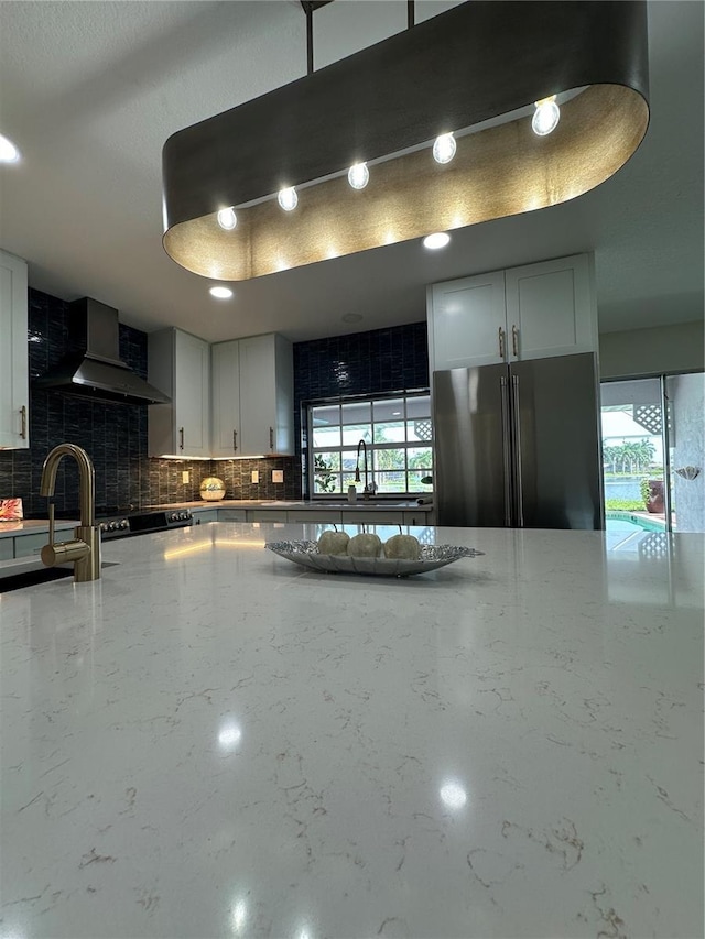 kitchen with black refrigerator, sink, white cabinets, and wall chimney exhaust hood