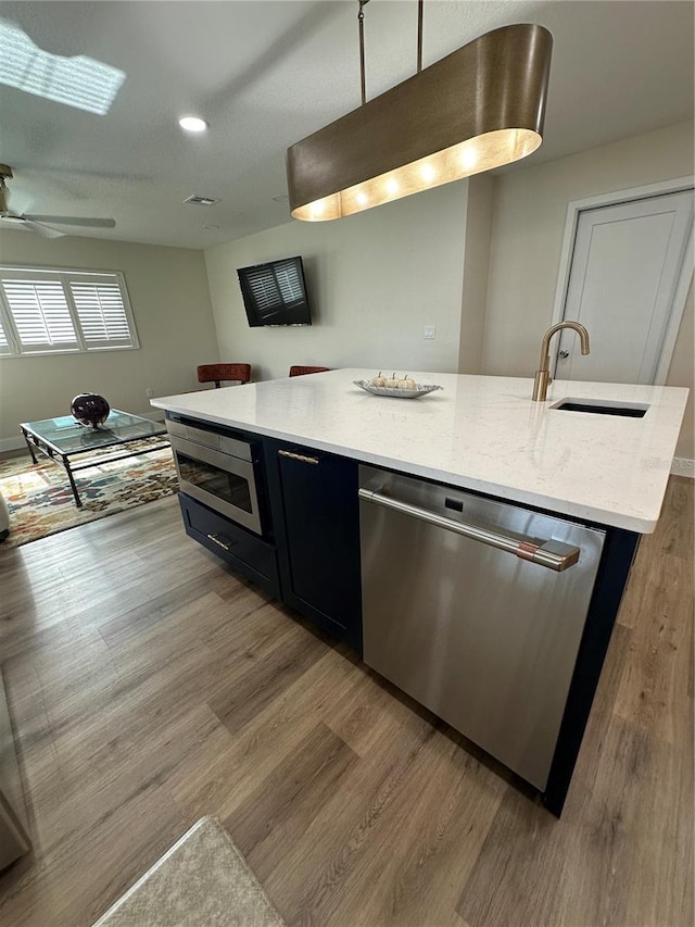 kitchen with sink, light stone counters, a center island with sink, light hardwood / wood-style flooring, and appliances with stainless steel finishes