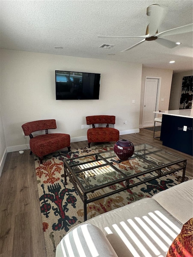 living room featuring dark hardwood / wood-style flooring, ceiling fan, and a textured ceiling