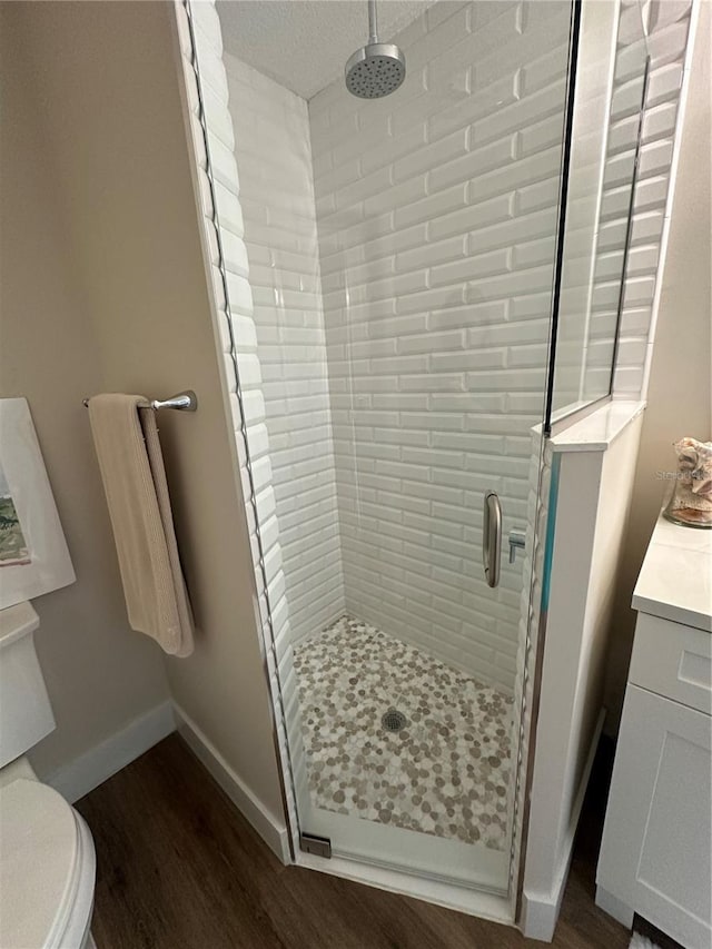 bathroom featuring wood-type flooring, toilet, a shower with shower door, and vanity