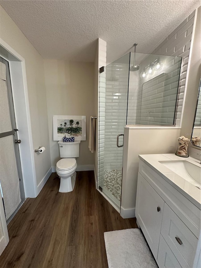 bathroom with hardwood / wood-style flooring, a shower with door, vanity, a textured ceiling, and toilet