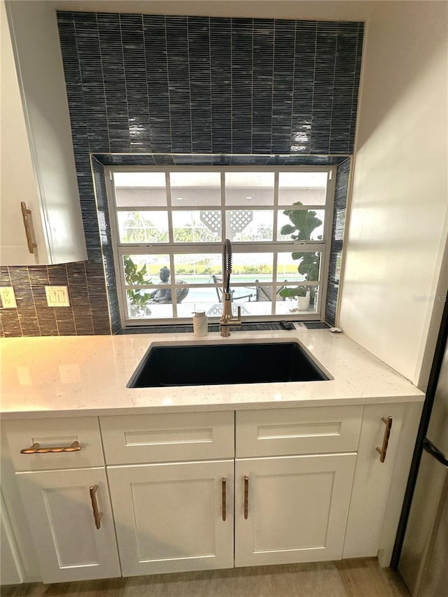 kitchen featuring light stone counters, sink, decorative backsplash, and white cabinets