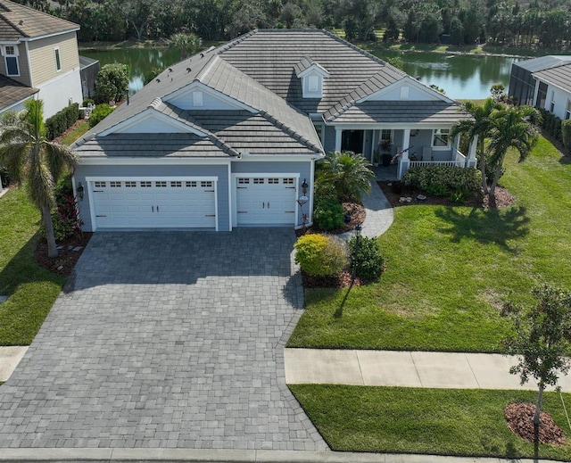 view of front of property with covered porch, a garage, a front lawn, and a water view