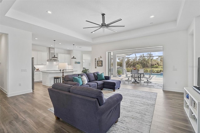 living room featuring ceiling fan, dark hardwood / wood-style flooring, and a tray ceiling