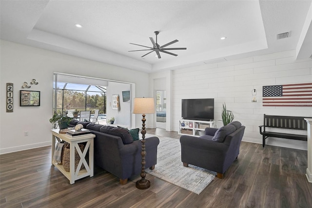 living room with a raised ceiling, dark hardwood / wood-style floors, and ceiling fan