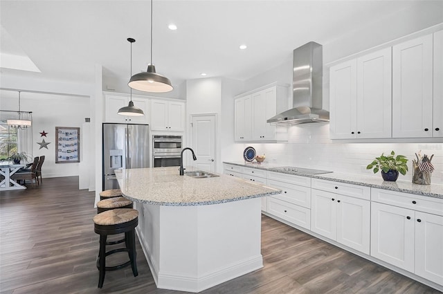 kitchen with appliances with stainless steel finishes, white cabinetry, an island with sink, sink, and wall chimney range hood