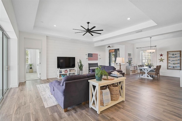 living room featuring a raised ceiling, wood-type flooring, and ceiling fan