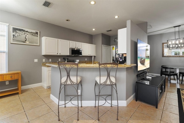 kitchen with a kitchen breakfast bar, light stone counters, white cabinets, decorative light fixtures, and kitchen peninsula