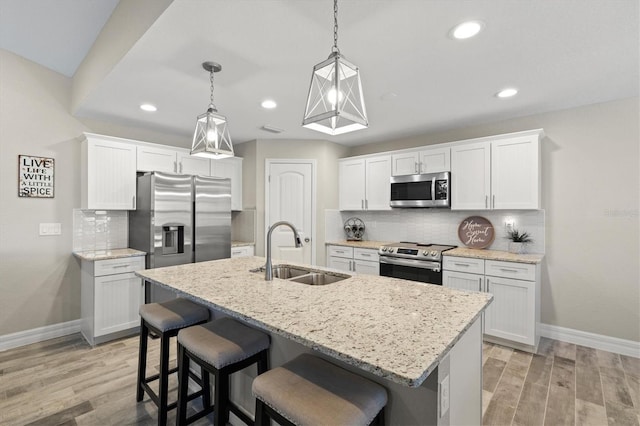 kitchen featuring pendant lighting, sink, white cabinetry, stainless steel appliances, and an island with sink