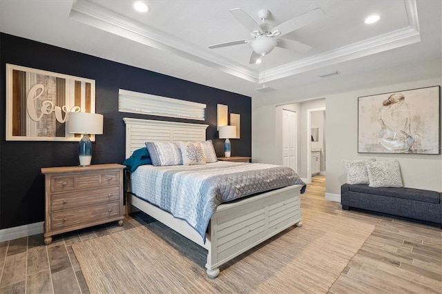 bedroom with ceiling fan, ornamental molding, a tray ceiling, and ensuite bath