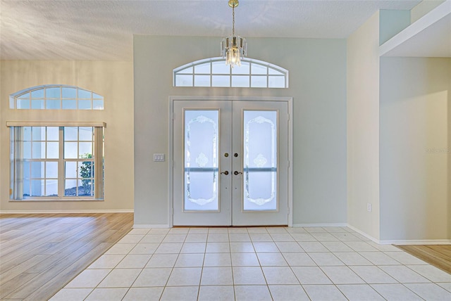 tiled foyer entrance featuring french doors, an inviting chandelier, and a textured ceiling