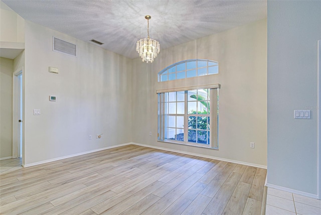 empty room with a textured ceiling, a chandelier, and light hardwood / wood-style flooring