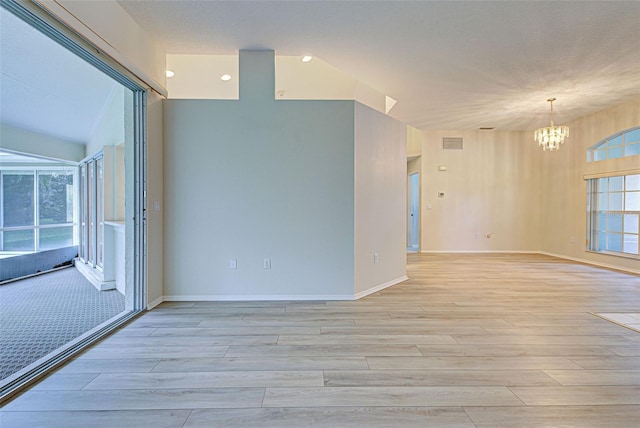 spare room featuring a healthy amount of sunlight, a notable chandelier, and light hardwood / wood-style flooring