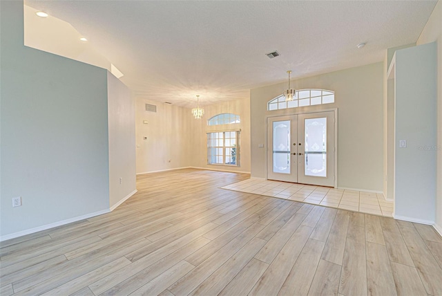 foyer entrance featuring an inviting chandelier, light hardwood / wood-style floors, and french doors