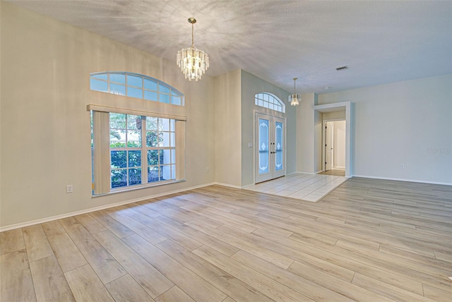 interior space featuring a notable chandelier, light hardwood / wood-style flooring, french doors, and a textured ceiling