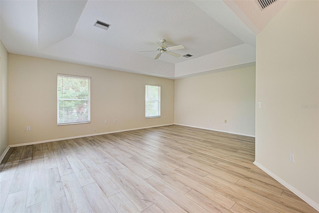 empty room with a healthy amount of sunlight, a tray ceiling, and light hardwood / wood-style flooring