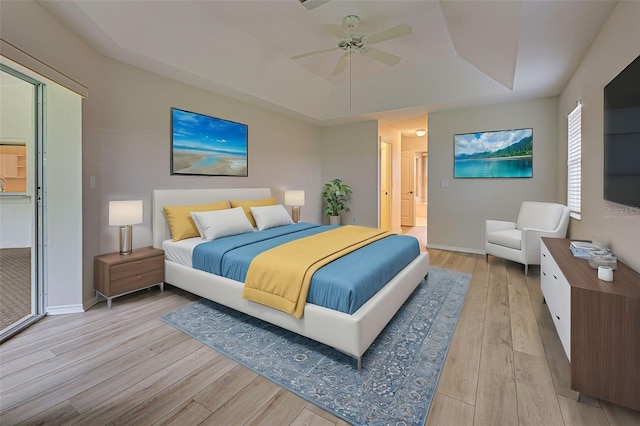 bedroom featuring ceiling fan, connected bathroom, a tray ceiling, and light hardwood / wood-style flooring