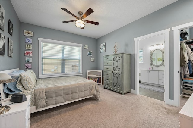 bedroom featuring ceiling fan, light colored carpet, ensuite bathroom, and a textured ceiling