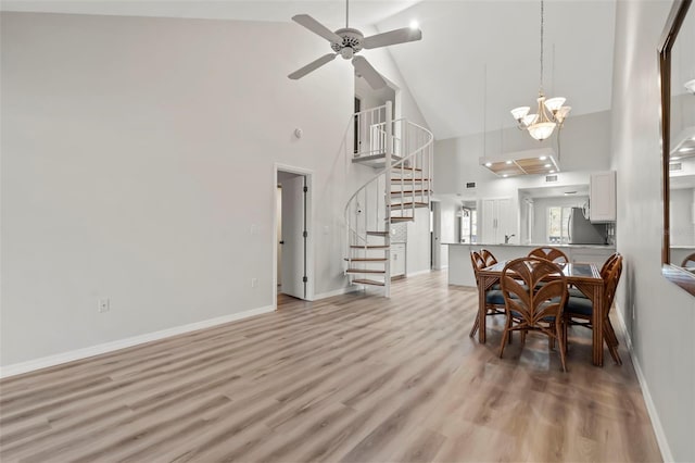 dining area with high vaulted ceiling, ceiling fan with notable chandelier, and light hardwood / wood-style floors