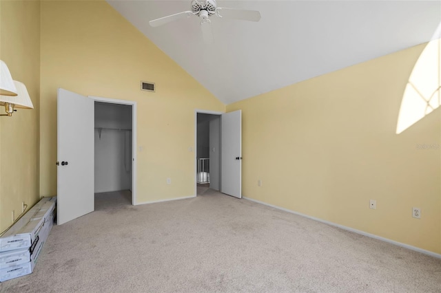 unfurnished bedroom with a walk in closet, light colored carpet, high vaulted ceiling, a closet, and ceiling fan