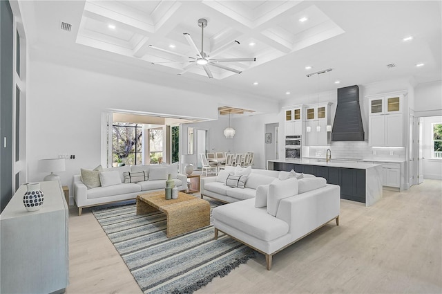 living room with coffered ceiling, sink, light hardwood / wood-style flooring, beamed ceiling, and a high ceiling