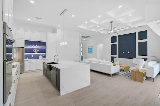 kitchen with pendant lighting, an island with sink, sink, white cabinets, and coffered ceiling