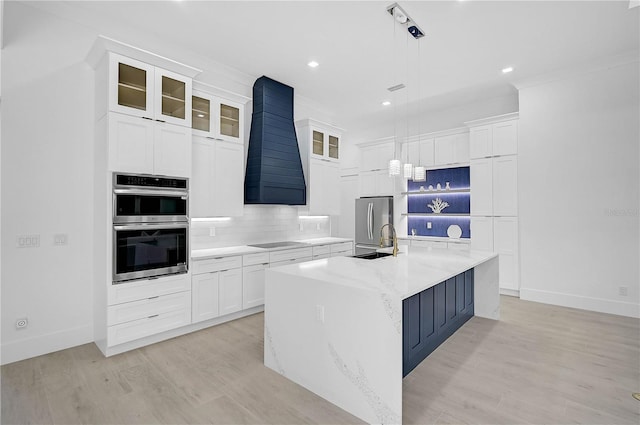 kitchen featuring appliances with stainless steel finishes, decorative light fixtures, a kitchen island with sink, and custom range hood