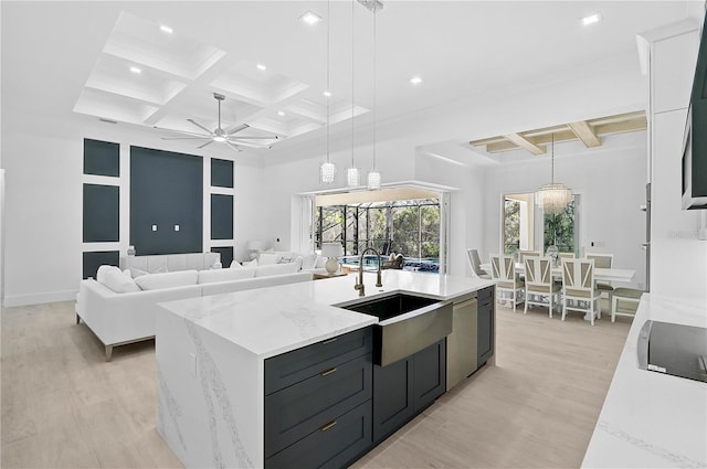 kitchen with sink, light hardwood / wood-style flooring, a kitchen island with sink, light stone countertops, and decorative light fixtures