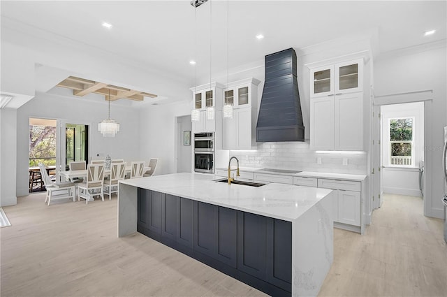 kitchen with a spacious island, custom exhaust hood, white cabinetry, hanging light fixtures, and black electric stovetop