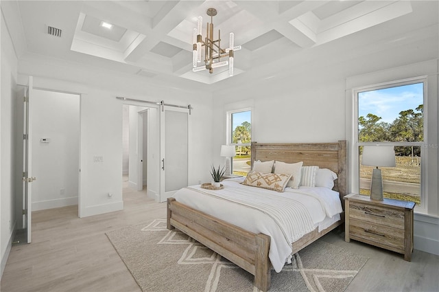 bedroom featuring multiple windows, light hardwood / wood-style flooring, coffered ceiling, and a barn door