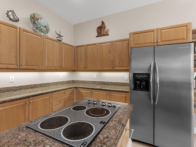 kitchen with dark stone countertops, stainless steel fridge with ice dispenser, and electric stovetop