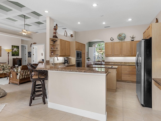 kitchen featuring a breakfast bar, stainless steel refrigerator, built in microwave, dark stone counters, and kitchen peninsula