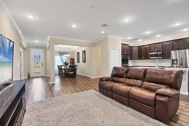 living area with ornamental molding, wood finished floors, visible vents, and baseboards