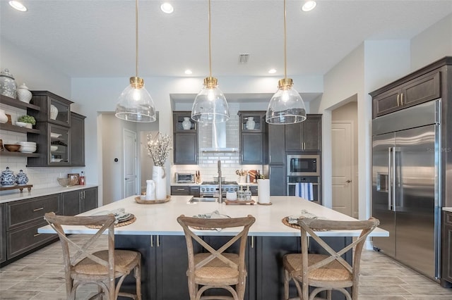 kitchen featuring dark brown cabinets, built in appliances, and a kitchen island with sink