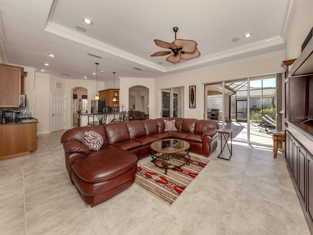 tiled living room with ceiling fan, ornamental molding, and a tray ceiling