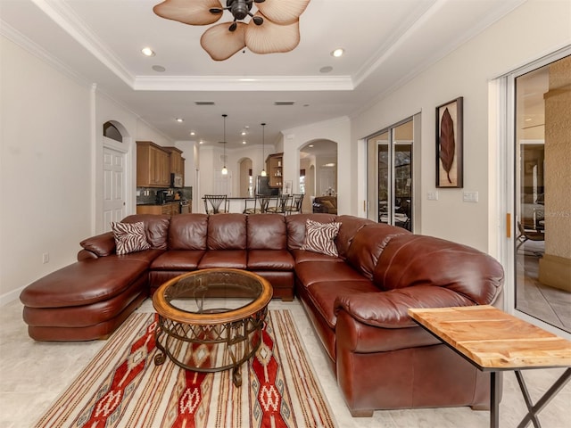 tiled living room with ceiling fan, ornamental molding, and a raised ceiling