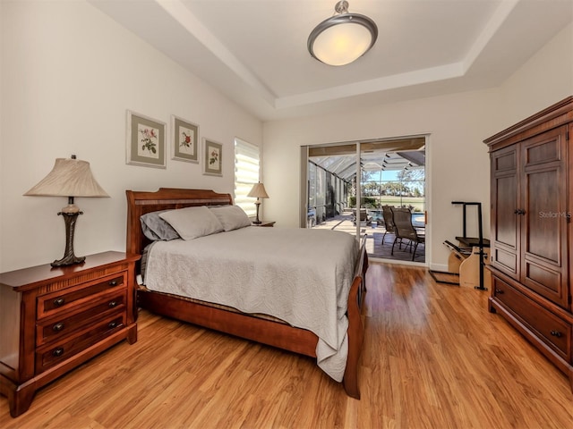 bedroom featuring light hardwood / wood-style flooring, a tray ceiling, and access to outside