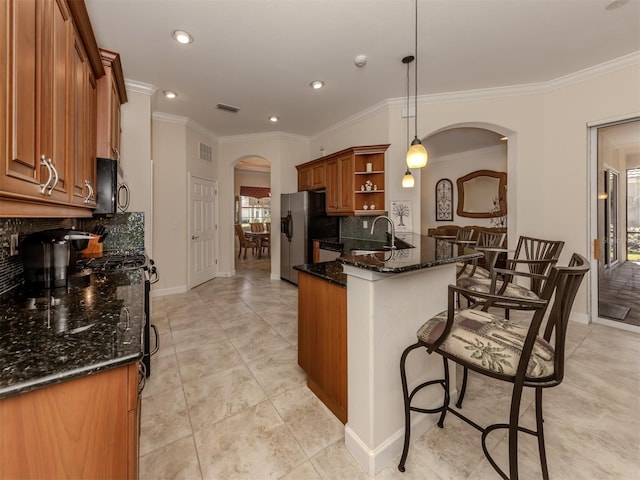 kitchen with decorative light fixtures, sink, dark stone countertops, stainless steel fridge, and kitchen peninsula