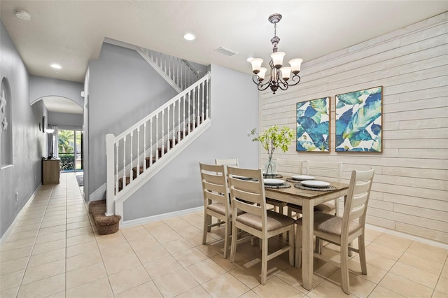 tiled dining space featuring an inviting chandelier and wood walls