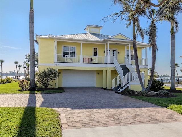 coastal inspired home featuring a garage, covered porch, and a front yard