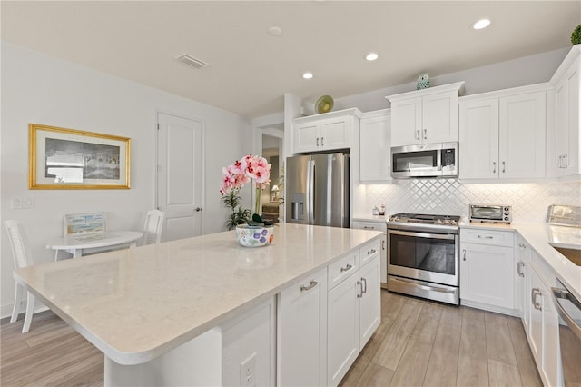 kitchen with a kitchen island, appliances with stainless steel finishes, white cabinetry, decorative backsplash, and light hardwood / wood-style floors