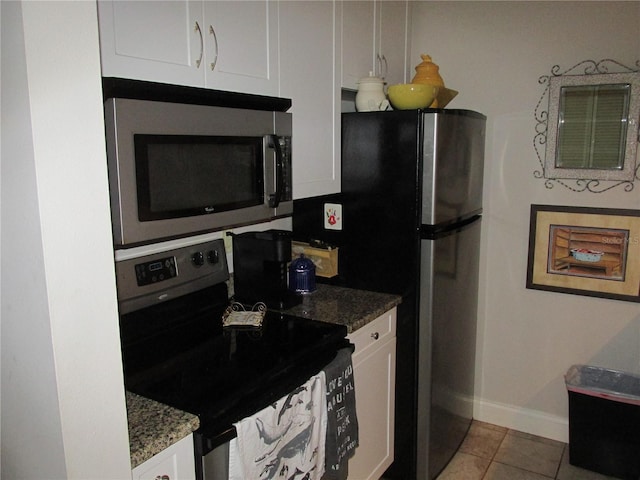 kitchen featuring light tile patterned floors, dark stone counters, white cabinets, and appliances with stainless steel finishes