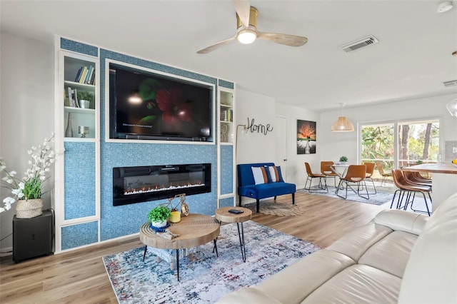 living room with ceiling fan, light wood-type flooring, and built in shelves