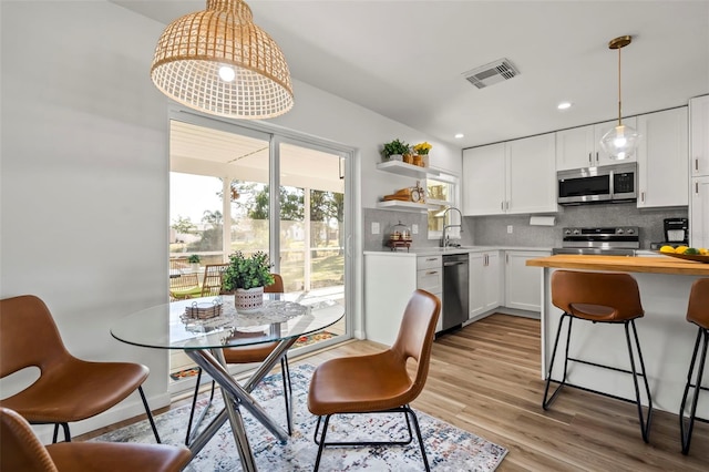 kitchen with sink, white cabinetry, stainless steel appliances, tasteful backsplash, and light hardwood / wood-style floors