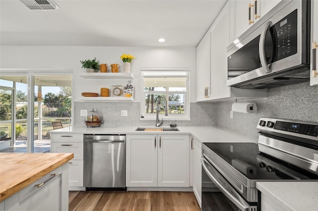 kitchen with white cabinetry, sink, stainless steel appliances, and butcher block counters