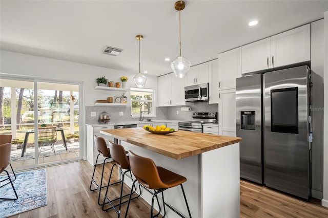 kitchen with wood counters, a breakfast bar, white cabinetry, a center island, and appliances with stainless steel finishes