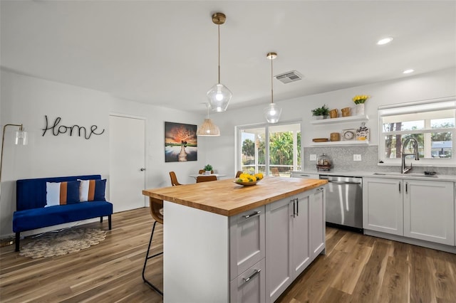 kitchen with wood counters, white cabinetry, stainless steel dishwasher, a kitchen island, and pendant lighting