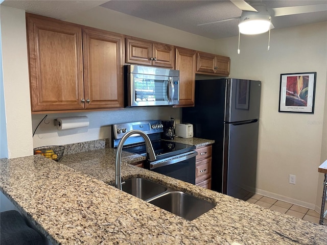 kitchen with sink, light tile patterned floors, kitchen peninsula, stainless steel appliances, and light stone countertops